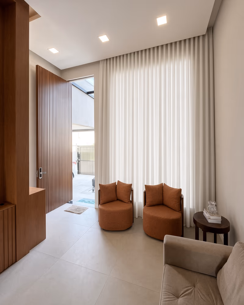 Hall de entrada com pé-direito duplo em Volta Redonda: cortina wave off-white do teto ao piso, poltronas terracota — projeto ShineCortinas